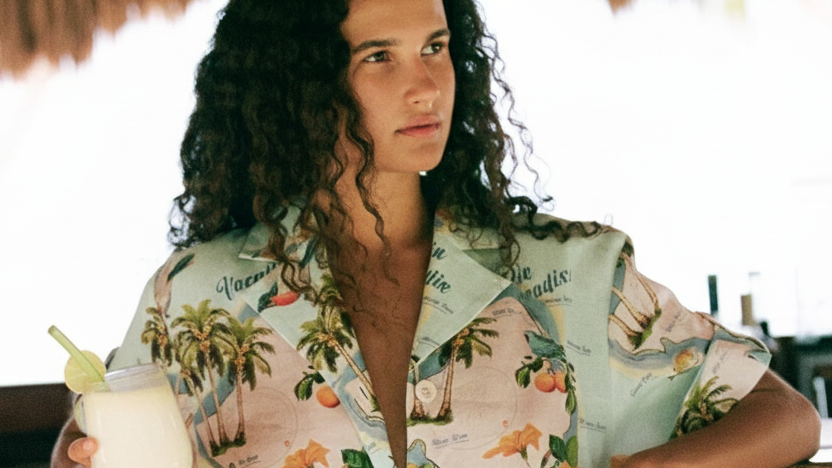 Woman in a tropical-themed Palm Noosa Dress holding a drink, standing in a casual outdoor setting. 